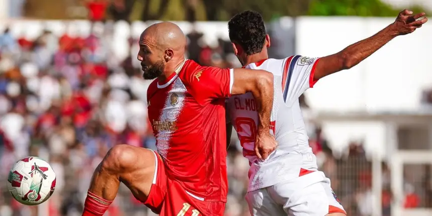 Renaissance Berkane player in red challenges a rival from Wydad Casablanca during a Moroccan league match, showcasing intense competition.