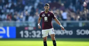Badr Benoun wearing Torino's maroon kit, standing on the pitch with fans in the background, during a Serie A match.