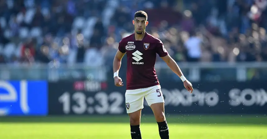 Badr Benoun wearing Torino's maroon kit, standing on the pitch with fans in the background, during a Serie A match.