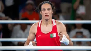 A determined Moroccan boxer in a red uniform with a national flag, standing in the ring, ready for competition.