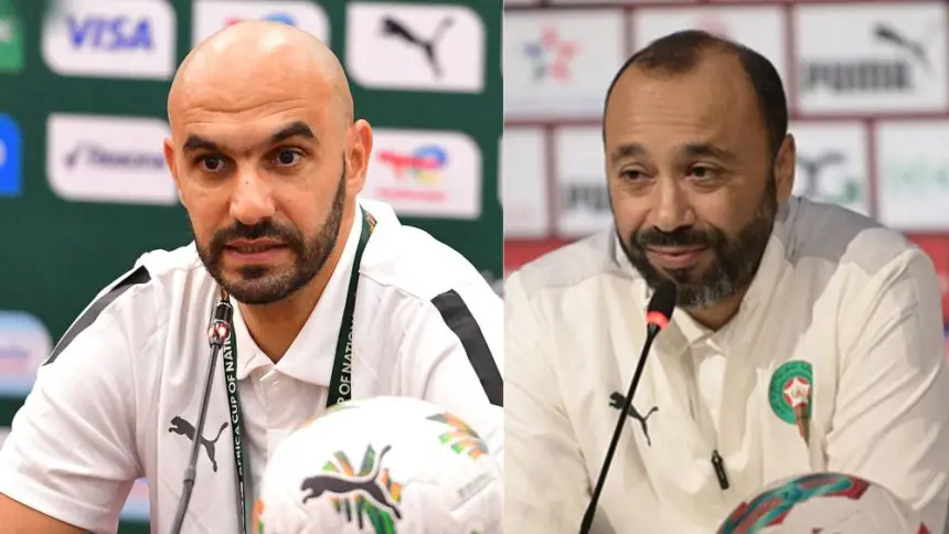 Twee voetbaltrainers in witte Puma-shirts, waarvan er één spreekt op een persconferentie, die het Marokkaanse voetbal vertegenwoordigen met het logo van het nationale team.