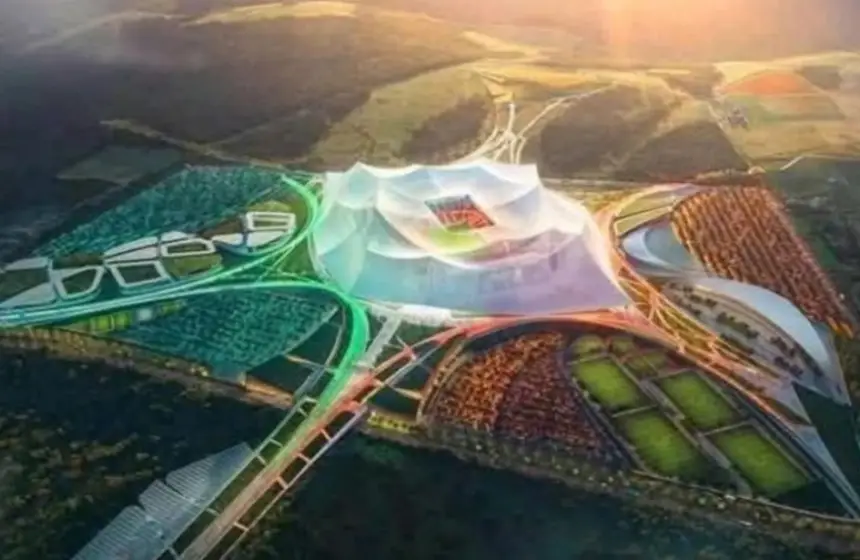 Aerial view of a modern stadium complex surrounded by greenery, featuring striking architecture and vibrant landscaping.