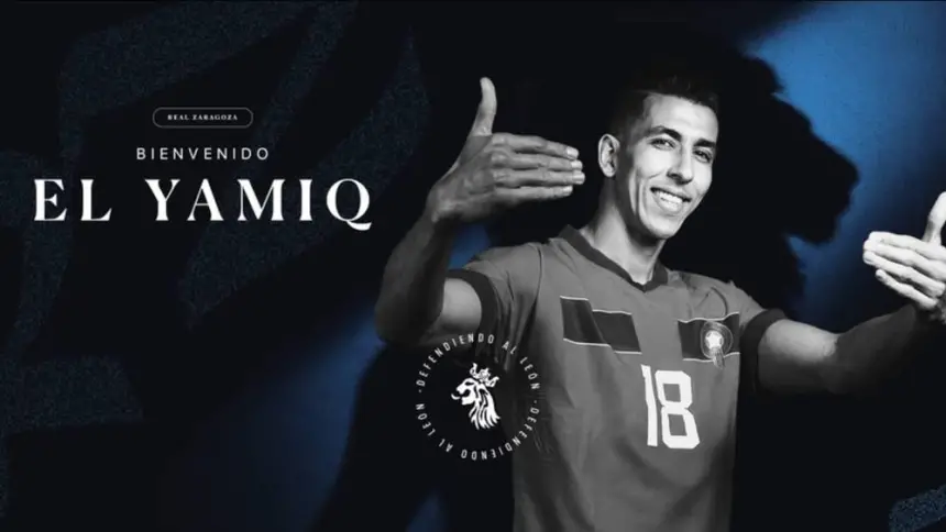 Moroccan footballer El Yamiq welcomes fans, wearing a blue and red jersey with the number 18, against a dramatic dark background.