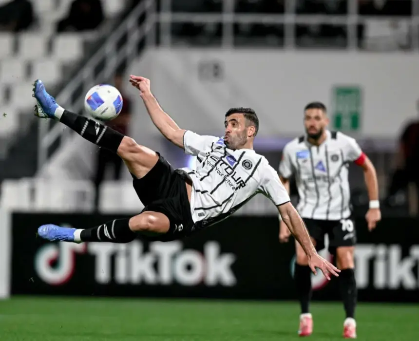 Moroccan player executing a spectacular overhead kick during a match, wearing a black and white team kit, with a teammate in the background.