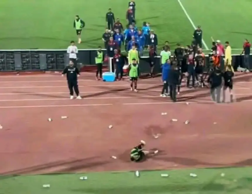Fans celebrate on the sidelines as a Moroccan football player sits on the pitch. Bottles litter the ground, capturing the match's intensity.