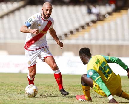 Moroccan player dribbling past a defender during a lively match, showcasing skill and determination on a sunlit pitch.