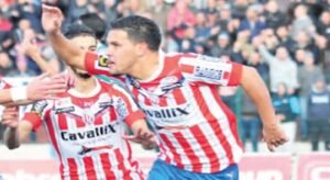 Celebrating players in red and white striped jerseys, with fans cheering in the background, capturing a thrilling football moment.