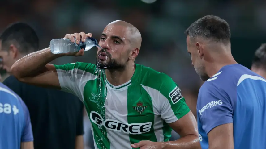 Sofyan Amrabat, in een groen-wit gestreept tenue, drinkt water tijdens een pauze in een wedstrijd met Real Betis.