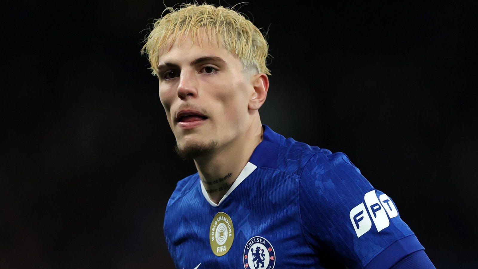 Alejandro Garnacho portant le maillot bleu de Chelsea, concentré pendant un match, arborant ses cheveux décolorés distinctifs et une expression intense.