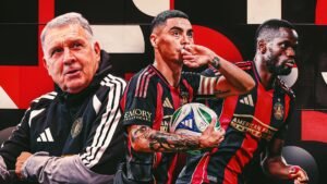 L'entraîneur principal d'Atlanta United, Gonzalo Pineda, sourit aux côtés des joueurs Miguel Almirón et Latte Lath, tous deux vêtus du maillot rayé rouge et noir emblématique de l'équipe.