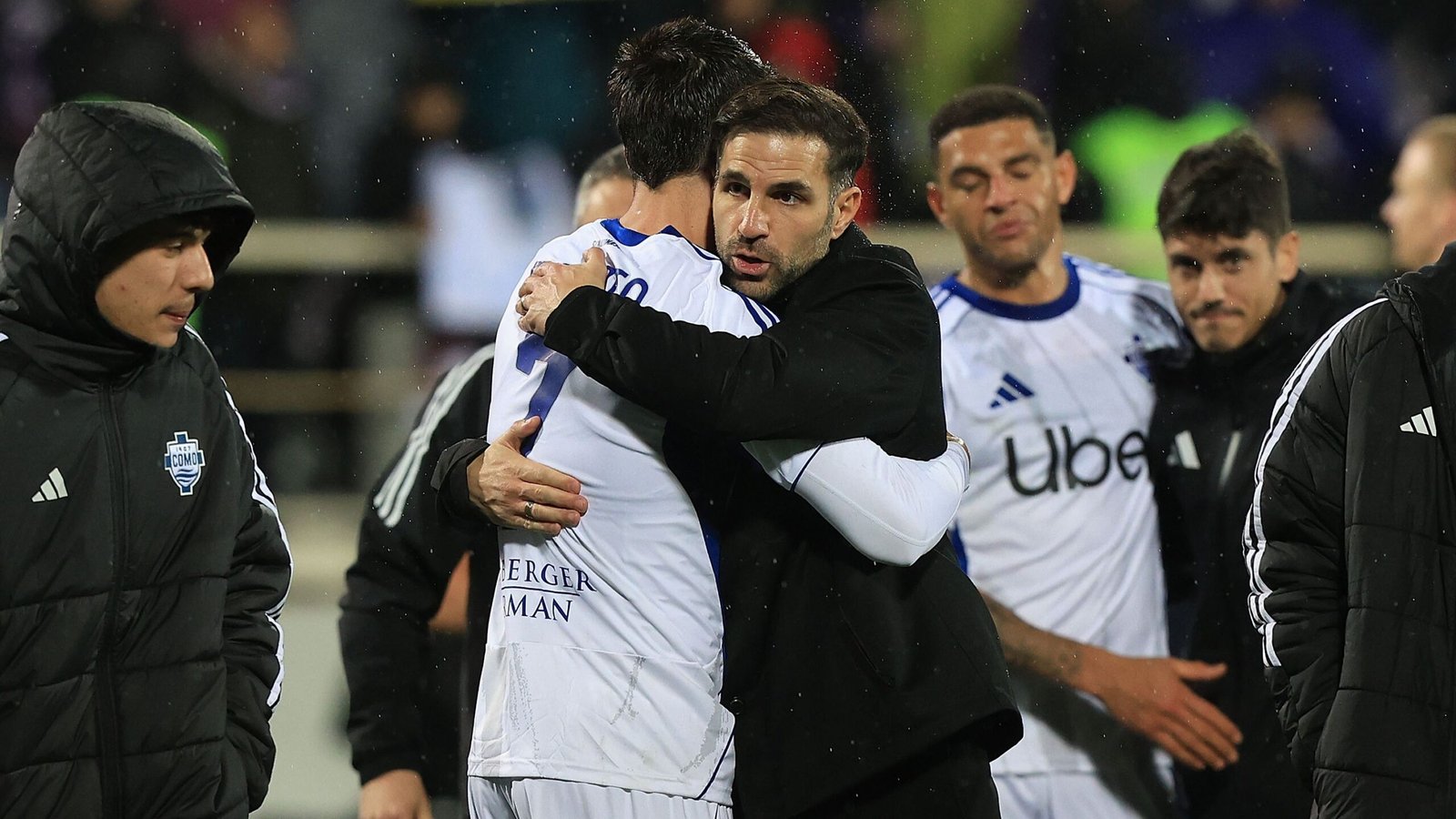 Alvaro Morata embraces Cesc Fabregas after a match, with teammates in the background, showcasing emotional support in football.