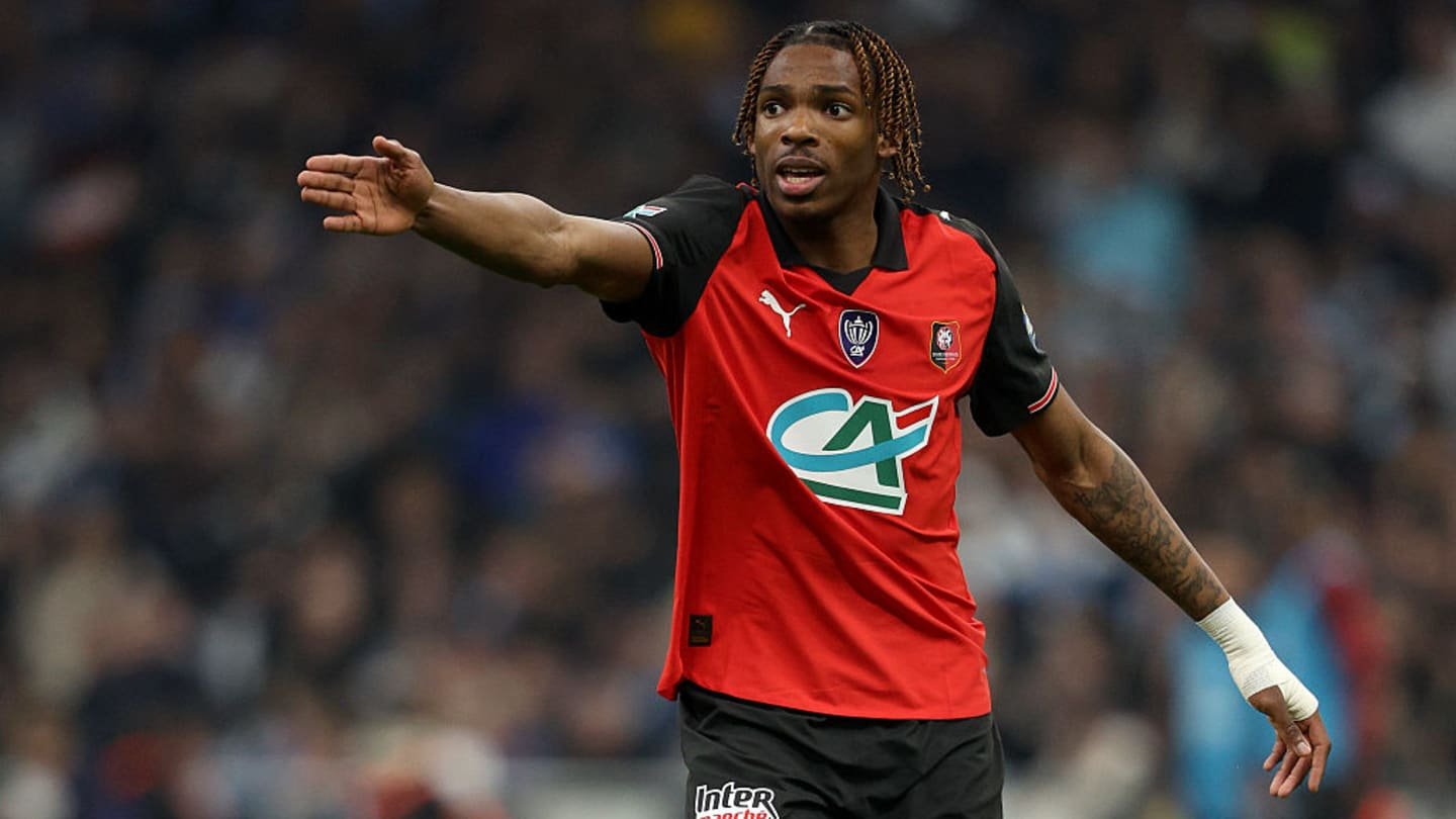 Jeremy Jacquet, wearing a red and black Rennes kit, gestures during a match, showcasing his leadership on the pitch.