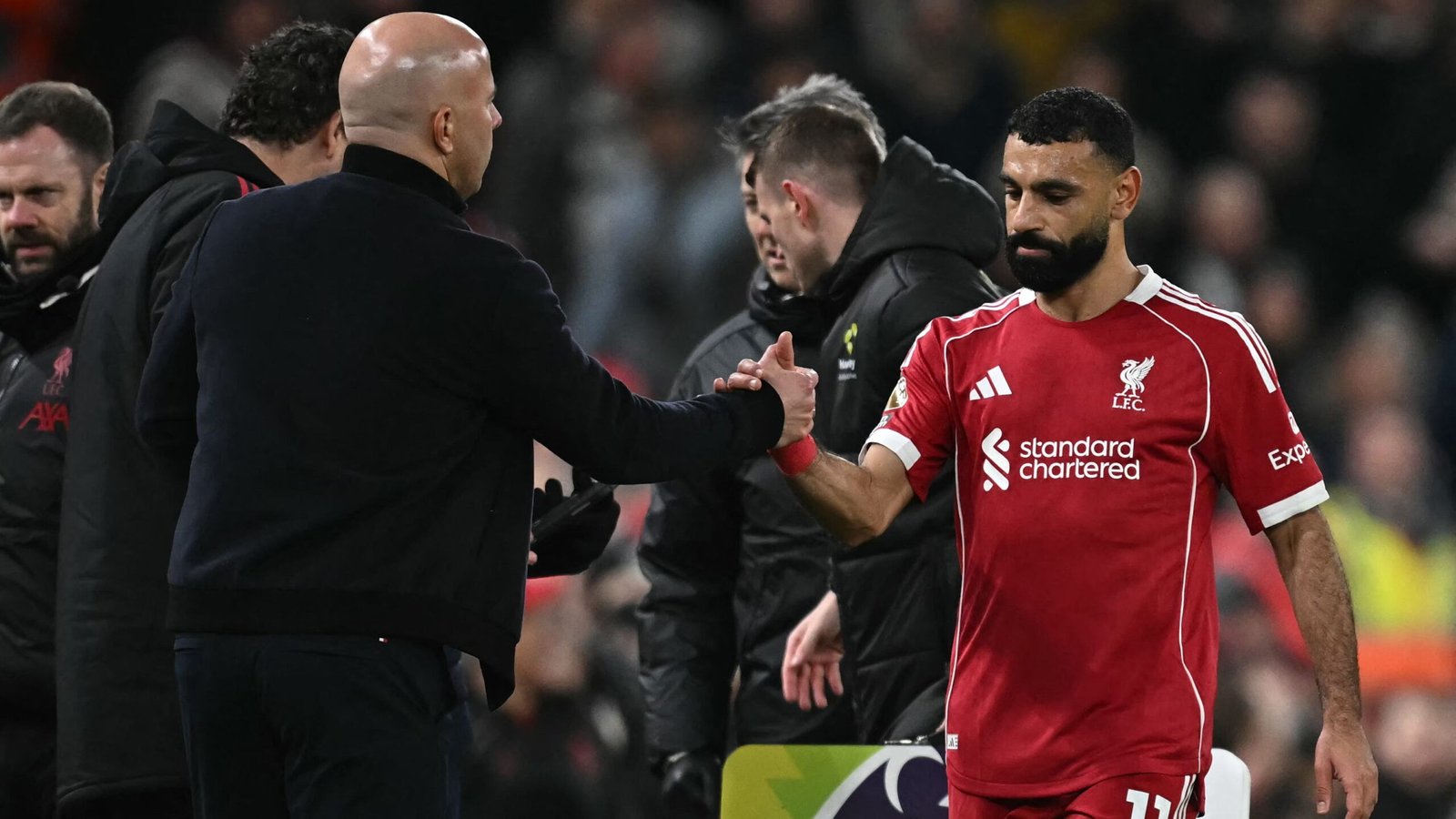 Arne Slot schudt Mohamed Salah de hand op het veld van Anfield, wat hun hernieuwde kameraadschap na het conflict benadrukt.