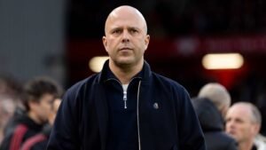 Arne Slot, Dutch football manager, stands focused on the sidelines during a match, wearing a navy jacket and expressing concentration.