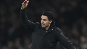 Mikel Arteta gesticue pendant un match, portant un manteau noir, mettant en lumière sa direction stratégique pour Arsenal avant le derby du nord de Londres.