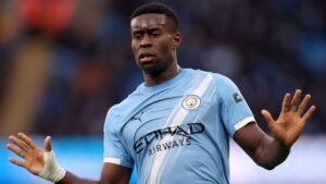 Nathan Aké dans le maillot bleu clair de Manchester City, gesticulant pendant un match, démontrant sa concentration et son leadership sur le terrain.