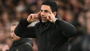 Le manager d'Arsenal, Mikel Arteta, gesticule avec passion en bord de touche lors d'un match, vêtu d'une veste noire au sein d'une foule enthousiaste.
