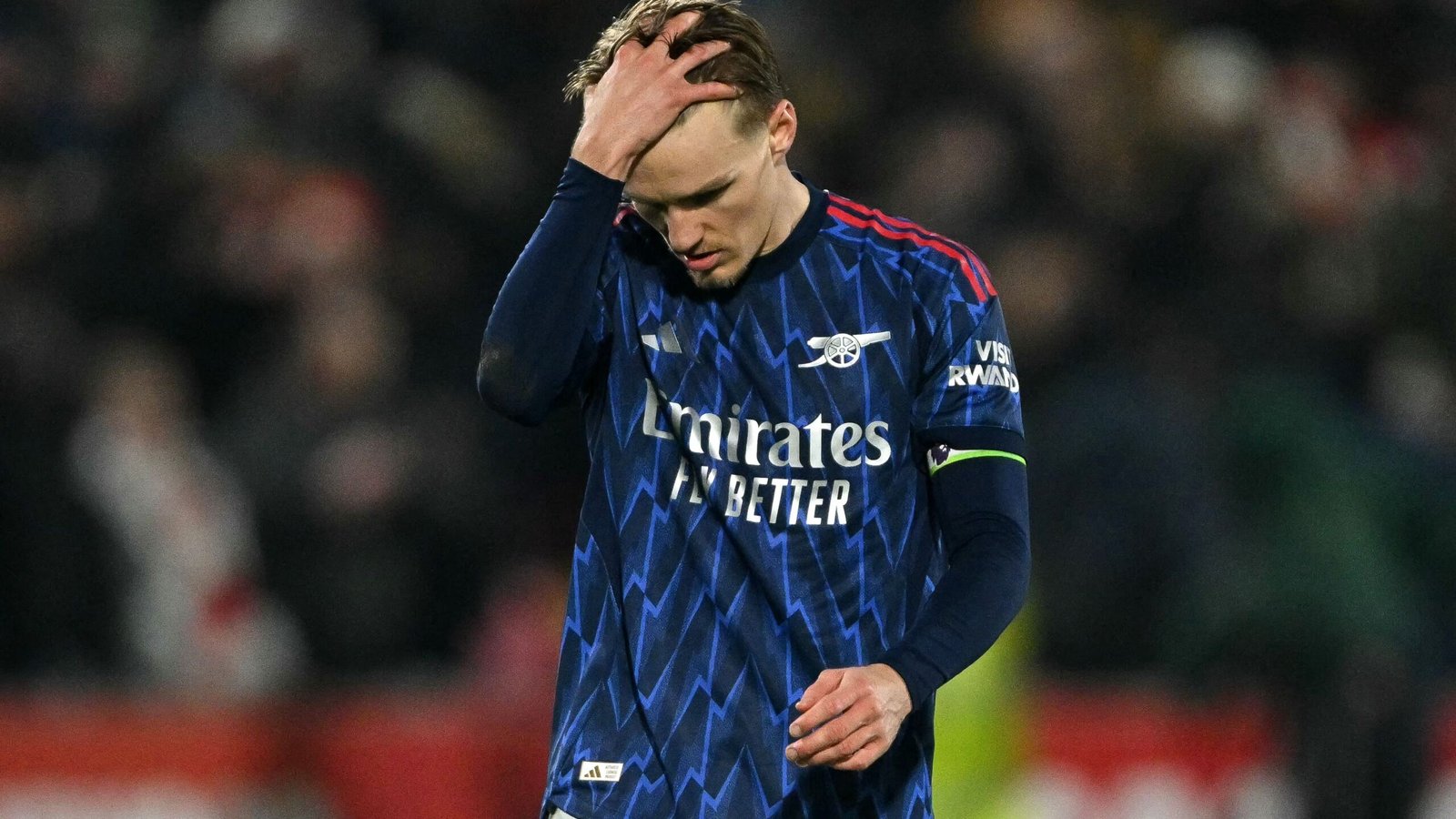 Arsenal's Martin Ødegaard looks dejected, holding his head, wearing the team's blue away kit during a match.