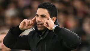 Mikel Arteta die gepassioneerd gebaart aan de zijlijn tijdens een Arsenal-wedstrijd, gekleed in een zwarte jas, en intense focus en vastberadenheid uitstraalt.