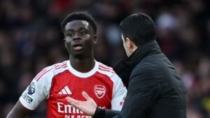 Arsenal's Bukayo Saka, in het rood-witte tenue van het team, luistert aandachtig naar manager Mikel Arteta tijdens een wedstrijdbespreking.