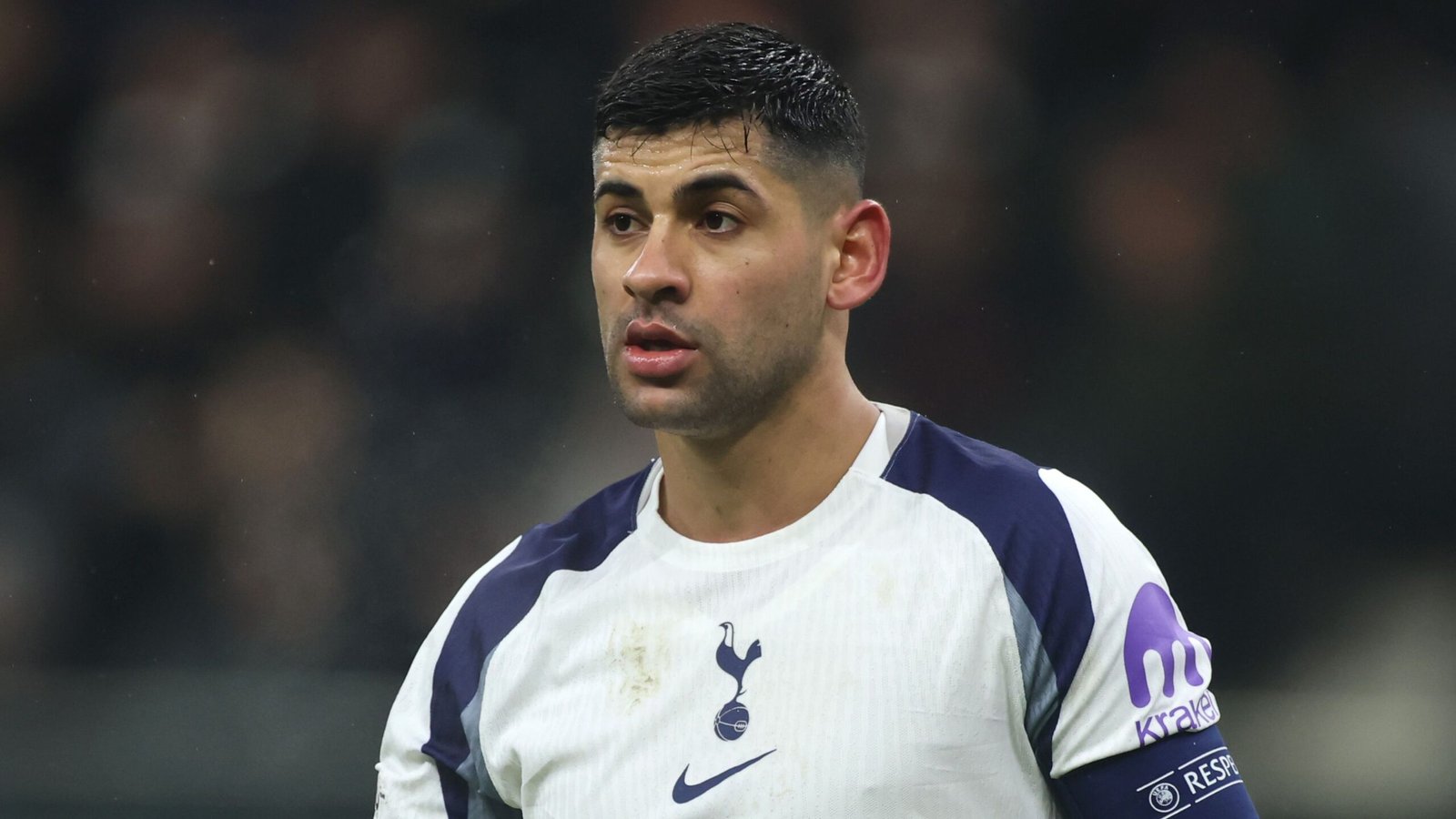 Le capitaine de Tottenham, Cristian Romero, apparaît concentré lors d'un match, portant un maillot blanc et marine sali, avec le logo des Spurs bien visible.