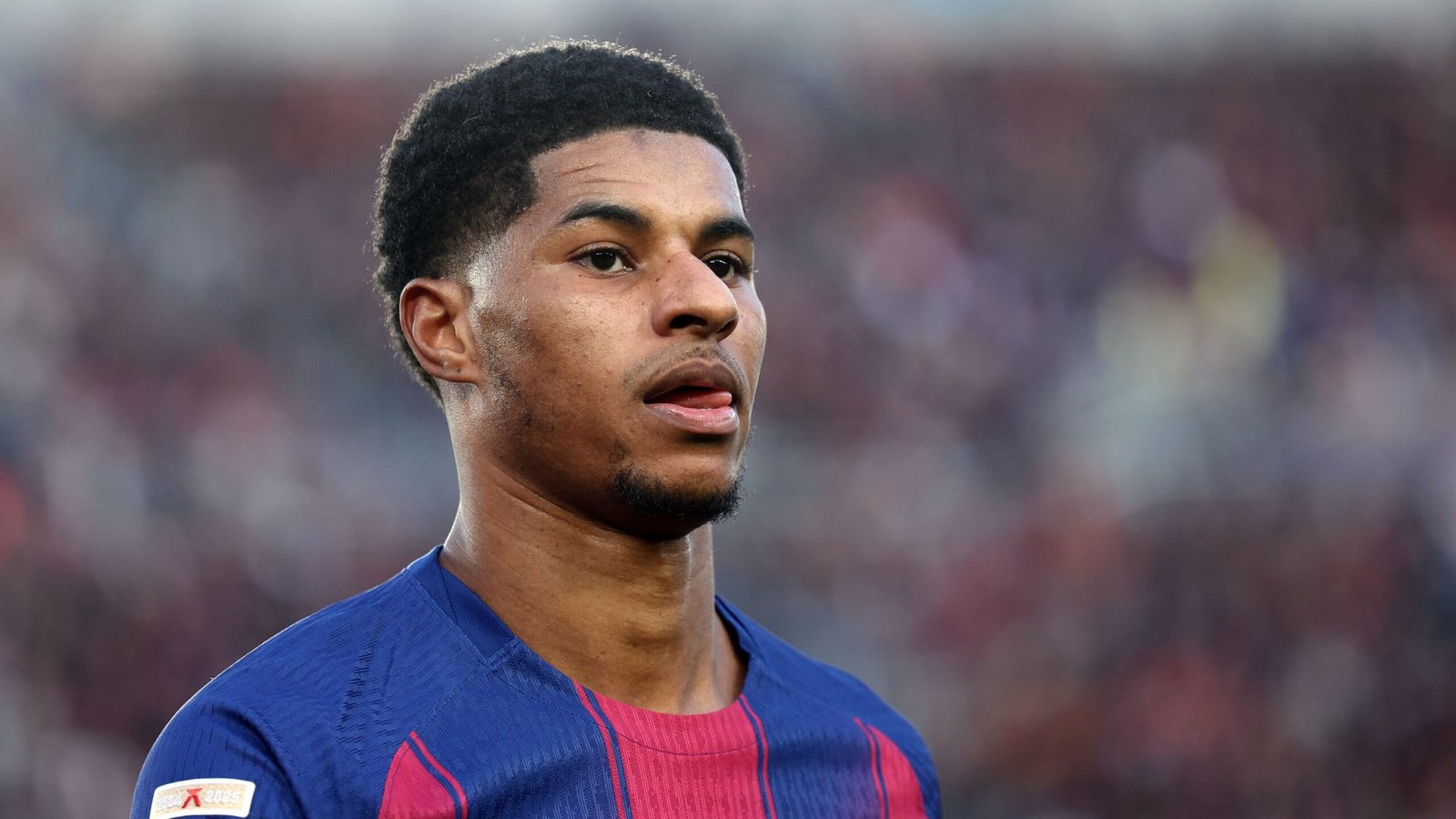 Marcus Rashford en tenue du Barça, affichant une expression concentrée pendant un match, mettant en avant les couleurs de l'équipe, le bleu et le grenat.