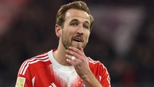 Harry Kane, en tenue du Bayern Munich, l'air pensif pendant un match, les couleurs rouge et blanche de l'équipe étant bien visibles en arrière-plan.