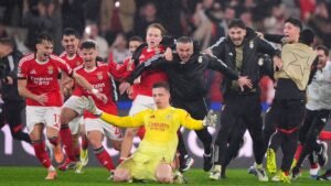 Benfica players and staff celebrate wildly around goalkeeper Trubin after a crucial match victory against Real Madrid.
