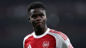 Bukayo Saka en tenue rouge et blanche d'Arsenal, affichant une expression concentrée pendant un match, soulignant son importance pour l'équipe.