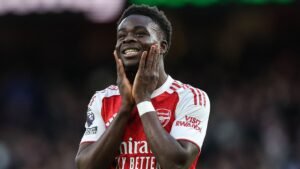 Bukayo Saka celebrating on the pitch in Arsenal's home kit, featuring red and white colours, showcasing his joy after a match.