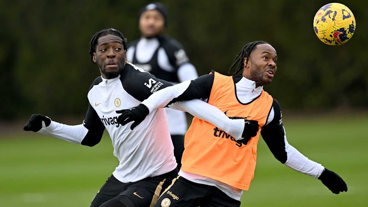 Two Chelsea players in training, one in an orange bib, the other in black and white, competing for the ball during a drill.