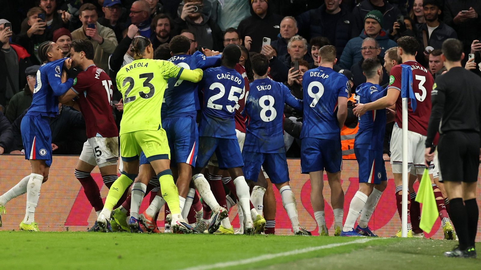 Les joueurs de Chelsea et de West Ham engagés dans une violente altercation pendant un match, entourés de supporters dans un stade animé.