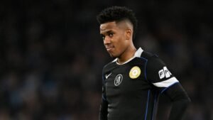 Estevao Willian portant un maillot de football noir avec un badge de club, l'air pensif pendant un match.