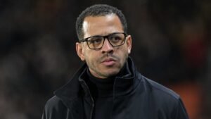Moroccan football manager in a dark jacket and glasses, reflecting on a match, showcases the intensity of coaching.