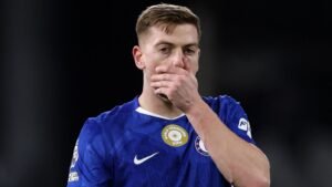 Liam Delap in Chelsea's blue kit looks dejected after a missed opportunity against Hull, highlighting a moment of disappointment.