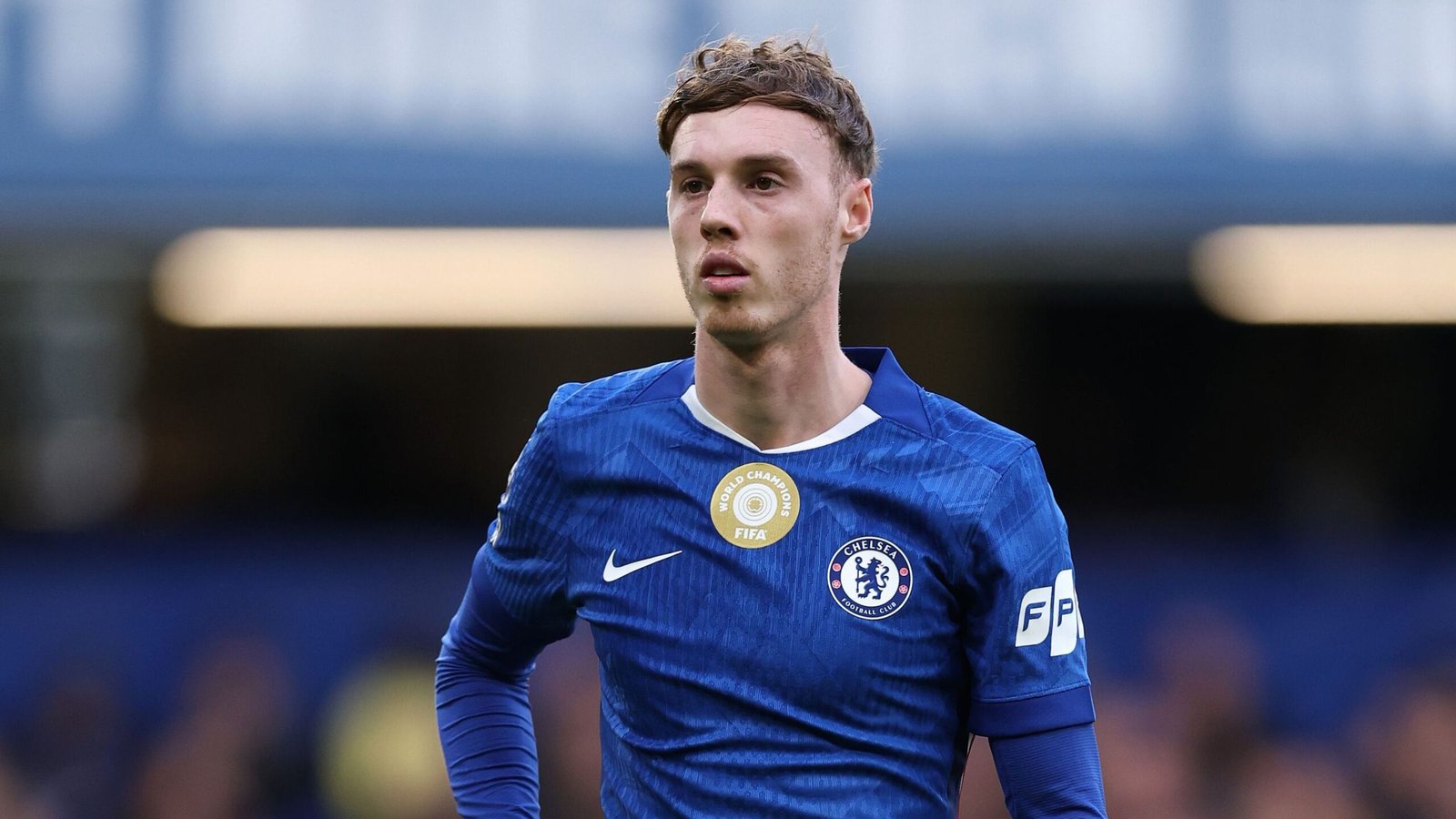 Chelsea's Cole Palmer in een blauw tenue, geconcentreerd kijkend tijdens een wedstrijd tegen een wazige stadionachtergrond.