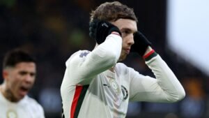 Cole Palmer viert met een hoofdtelefoongebaar, gekleed in het tenue van het Engelse nationale team, tijdens een wedstrijd te midden van teamvieringen.