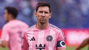 Lionel Messi in a pink Inter Miami kit, looking focused during a match, with teammates blurred in the background.