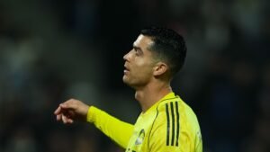Cristiano Ronaldo portant le maillot jaune d'Al-Nassr, l'air pensif pendant un match, arborant sa coupe de cheveux iconique et une expression concentrée.