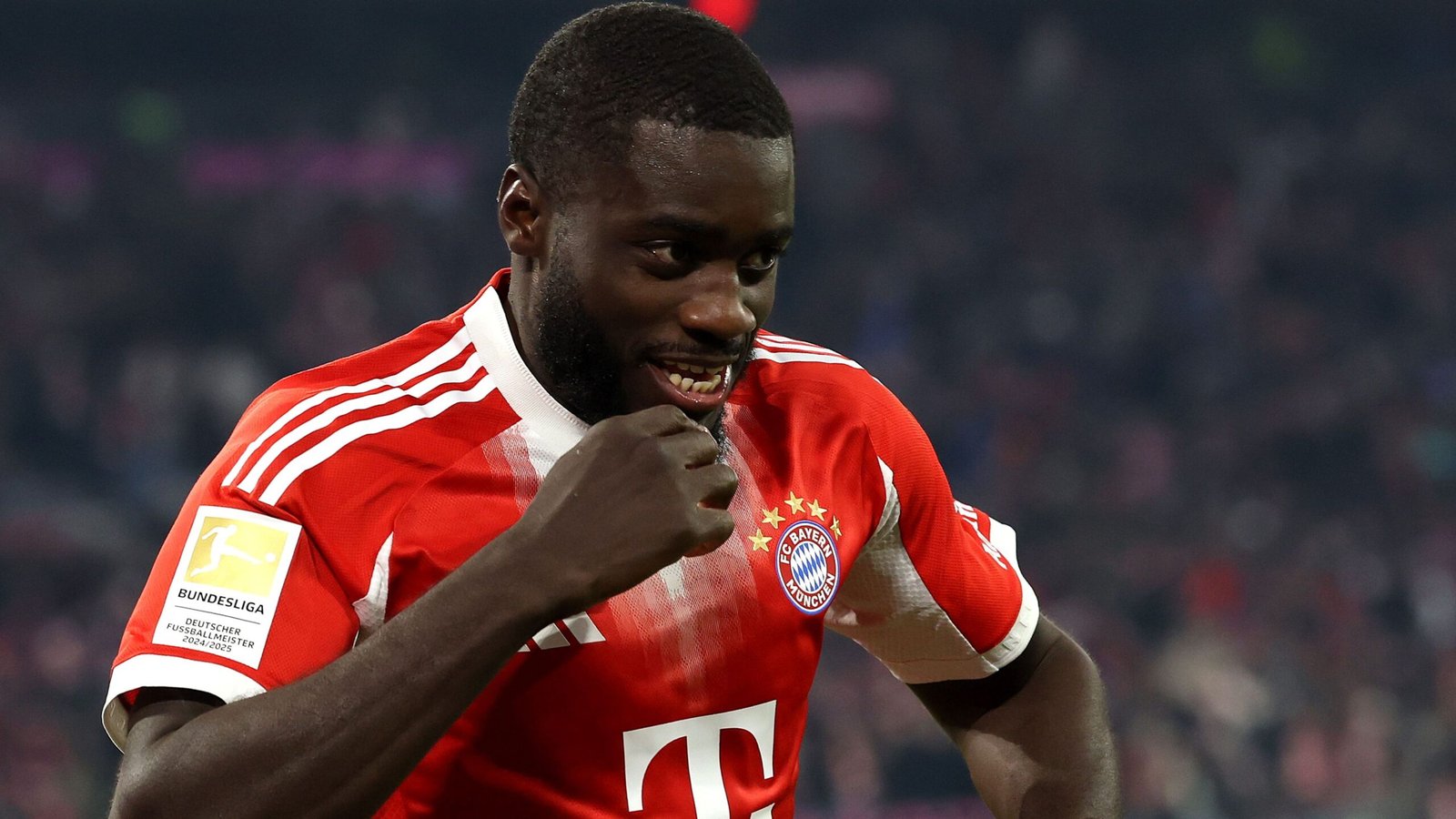 Dayot Upamecano in Bayern Munich's red home kit celebrates in the stadium, highlighting his joy after a match victory.