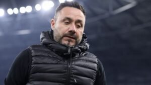 De Zerbi, vêtu d'une doudoune noire, semble contemplatif après la défaite de Marseille contre le PSG, sous les projecteurs du stade.