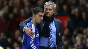 Eden Hazard in a blue Chelsea kit receives guidance from manager José Mourinho, both engaged in a critical moment on the pitch.