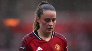 Ella Toone in een Manchester United-shirt, somber kijkend tijdens een regenachtige wedstrijd, wat haar teleurstelling over het missen van belangrijke wedstrijden benadrukt.