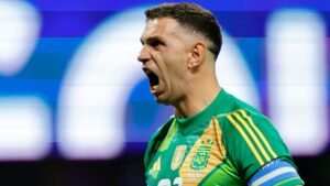 Emiliano Martínez, vêtu de la tenue verte de gardien de but de l'Argentine, crie avec ferveur pendant un match, montrant une détermination et une passion intenses.