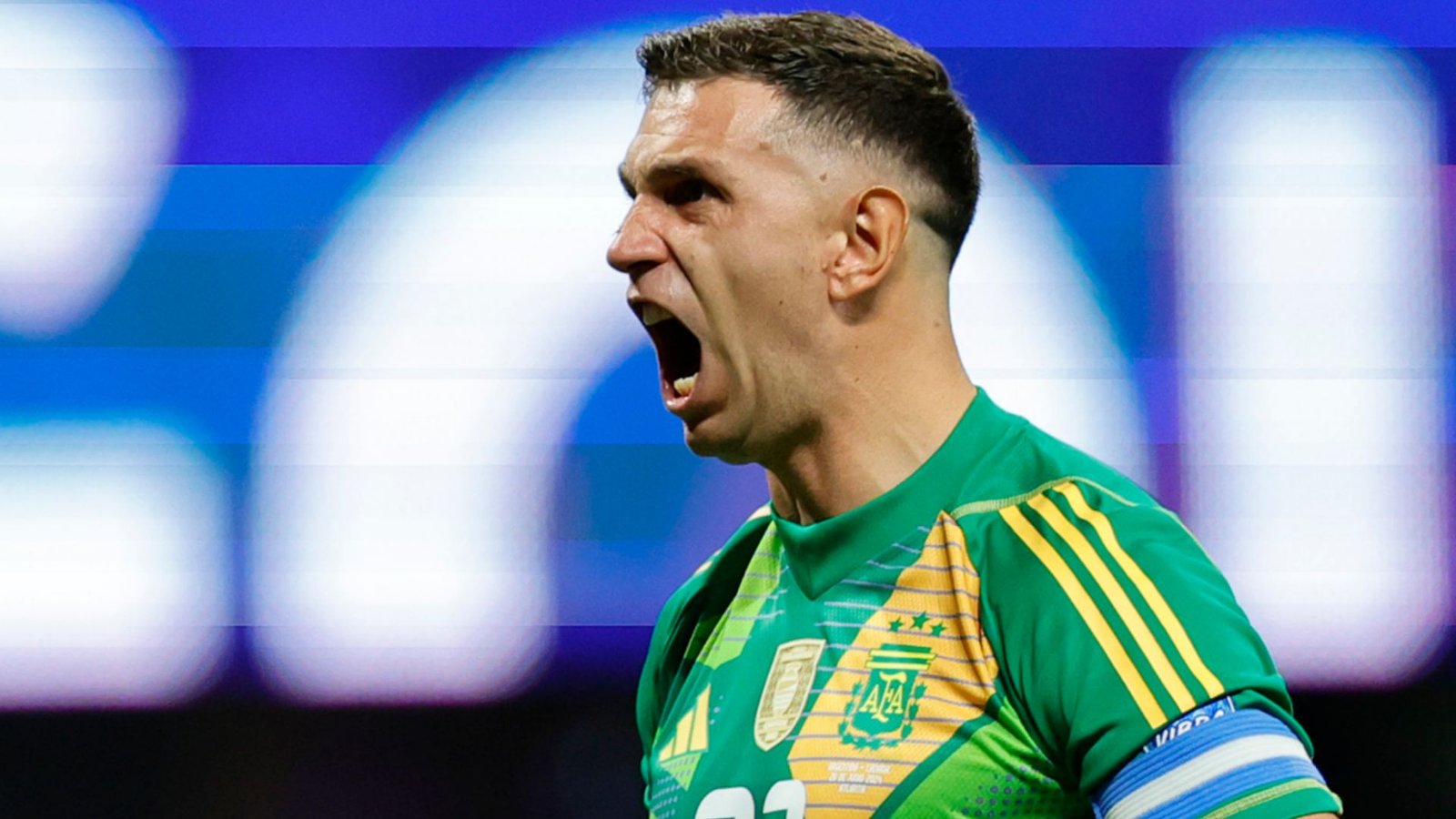 Emiliano Martínez, vêtu de la tenue verte de gardien de but de l'Argentine, crie avec ferveur pendant un match, montrant une détermination et une passion intenses.