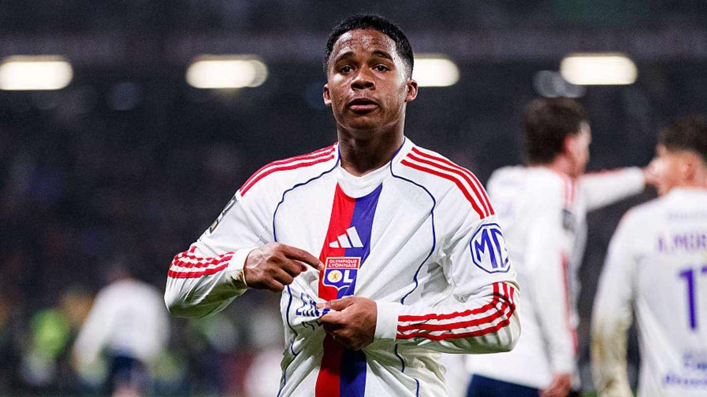 Lyon player showing his jersey, celebrating a moment on the pitch during a Ligue 1 match, with teammates in the background.