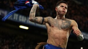 Célébrant avec passion, Enzo Fernandez brandit son maillot bleu, dévoilant ses tatouages, dans une atmosphère de stade vibrante.