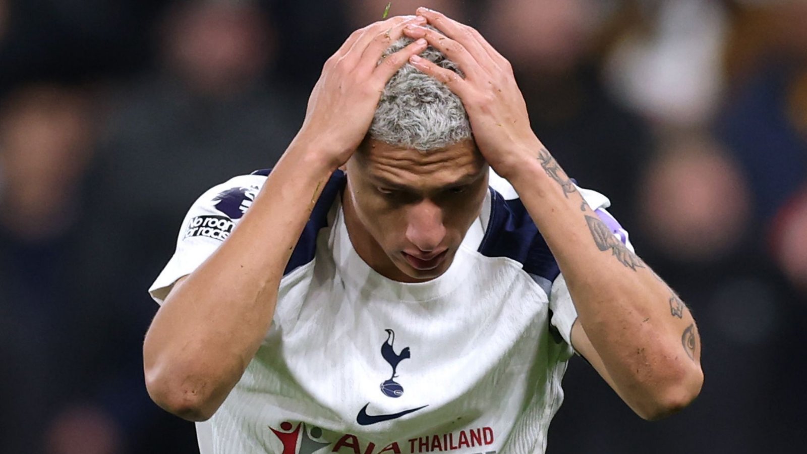 Richarlison, in a white Tottenham kit, holds his head in despair during a match, highlighting a moment of frustration for the team.