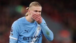 Erling Haaland, vêtu du maillot bleu ciel de Manchester City, une main devant la bouche, affiche une concentration intense pendant un match.