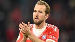 Harry Kane, gekleed in het rode tenue van Bayern München, klapt waarderend na een wedstrijd, wat zijn focus en toewijding op het veld illustreert.